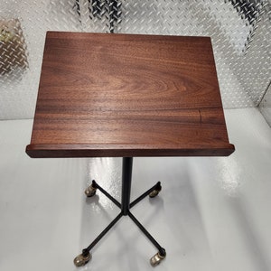 May include: A wooden lectern with a dark brown finish and a black metal base with four wheels. The lectern is on a white surface.
