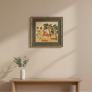 May include: A square framed wall art piece featuring a stylized illustration of a person on horseback accompanied by a dog in a landscape with trees. The artwork is enclosed in a dark green mat and a textured gold-toned frame, creating a classic look.