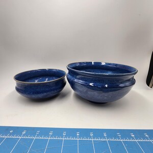 May include: Two blue ceramic bowls, one larger than the other, with a speckled glaze. The bowls are sitting on a blue cutting mat.