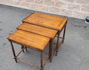 May include: A set of three nesting tables with a wood grain finish and a simple, elegant design. The tables are made of wood and have a dark brown color.