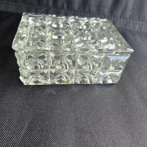 May include: A rectangular clear glass box with a lid, featuring a repeating geometric pattern of raised circular indentations within square frames across the top and sides, creating a textured, multifaceted appearance.