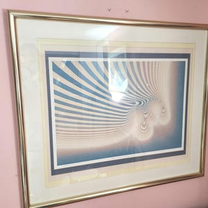May include: A framed abstract print with a blue, white and beige colour scheme. The print features a swirling, optical illusion design.