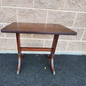 May include: A dark brown wooden table with a rectangular top and a simple, elegant design. The table has four legs with a curved design and a single stretcher.