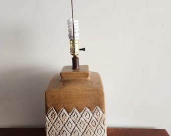 May include: A brown ceramic table lamp with a white geometric pattern. The lamp has a black metal shade and a white light bulb.