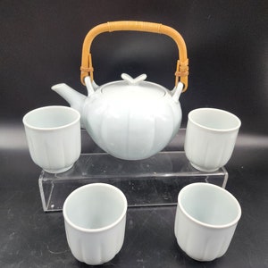 Puede incluir: Una tetera de cerámica blanca con asa de bambú y cuatro tazas de té a juego. La tetera tiene un diseño acanalado y una forma redondeada.