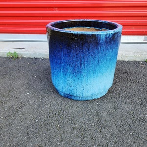 May include: A blue and black ceramic planter with a glazed finish. The planter has a faded blue and white ombre effect.