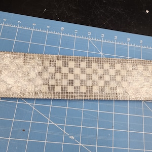 May include: A close-up of a rectangular piece of white and grey mosaic tile. The tile is wrapped in clear plastic and has a chequered pattern.