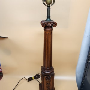 Puede incluir: Una lámpara de madera con una base en forma de columna y un diseño floral tallado. La lámpara tiene un casquillo de latón y una pantalla de vidrio transparente.