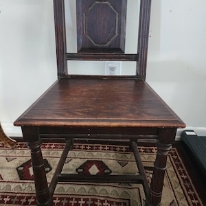 Könnte beinhalten: Ein dunkelbrauner Holzstuhl mit geschnitzter Rückenlehne und gedrehten Beinen. Der Stuhl hat ein schlichtes Design und ist in gutem Zustand.