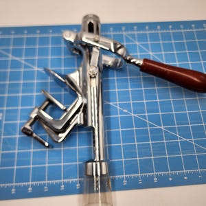 May include: A silver and brown metal wine bottle opener with a clear plastic tube on the bottom. The opener is on a blue cutting mat.