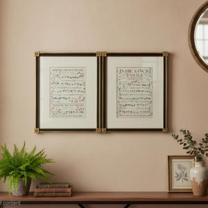 May include: Two rectangular wall frames with black and gold borders containing off-white paper sheets with printed musical notation and Latin text. The left sheet features the text Dominica Adest and the right sheet features In Die Sancto Paschae.