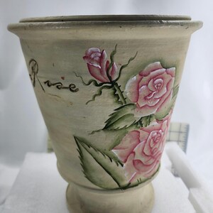Può includere: Fioriera in ceramica beige, dipinta a mano con rose rosa e foglie verdi. La parola "Rose" è scritta in corsivo sul lato. La fioriera ha una forma leggermente svasata.