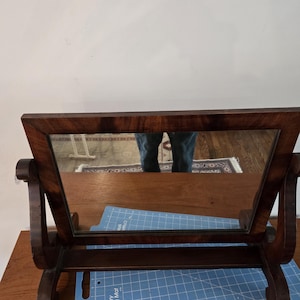 Puede incluir: Un espejo de tocador con marco de madera oscura y espejo de vidrio biselado. El espejo está sobre una estera de corte azul.