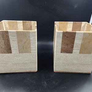May include: Two square-shaped beige and brown stone wastebaskets with a striped pattern.