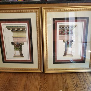 May include: Two framed prints of architectural details, each featuring a column with intricate carvings and a gold-colored frame.