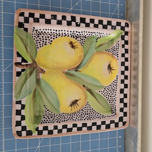 May include: A square ceramic serving platter with a black and white checkered border. The center of the platter features a hand-painted design of three yellow pears with green leaves on a pink background with black polka dots.