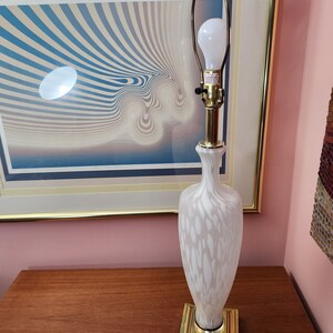 Può includere: Una lampada da tavolo in vetro bianco con una base dorata e un paralume bianco. La lampada ha un design bianco e oro.