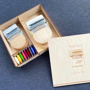 以下が含まれることがあります： 2つの小さな織機、色とりどりの糸のセレクション、木製の蓋が入った木箱セット。蓋には「Small Loom」、「Darning」、「Alexon Ver」の文字が刻まれています。織機は金属製の歯と木製のベースを備えています。