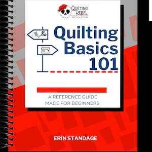 May include: A white book cover with a red and black skull logo that says "Quilting Rebel" and the text "Quilt with Attitude". The title of the book is "Quilting Basics 101" with a red dashed line underneath. The book cover also includes two signs with sewing and quilting symbols. The text "A Reference Guide Made for Beginners" is below the title. The author's name, "Erin Standage", is at the bottom of the cover.