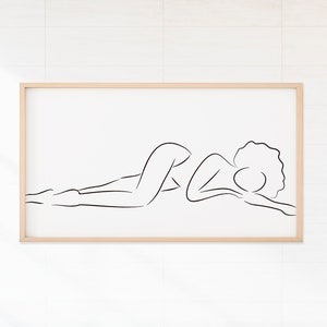 Puede incluir: Un dibujo en blanco y negro de una persona acostada, enmarcado en un marco de madera clara, colgado en una pared de azulejos blancos.