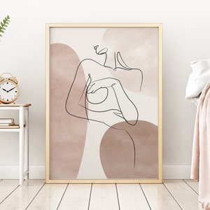 Puede incluir: Un dibujo de l&iacute;nea minimalista de una persona con un cuerpo desnudo, sobre un fondo de formas abstractas en tonos rosa y marr&oacute;n. La obra de arte est&aacute; enmarcada en un marco dorado.