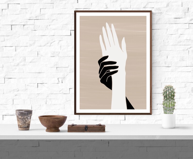 Puede incluir: Una impresi&oacute;n de arte abstracto enmarcada que presenta dos manos, una negra y una blanca, superpuestas sobre un fondo beige.