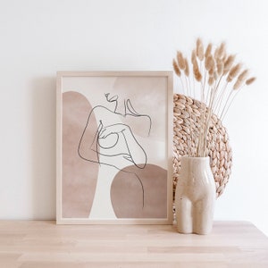 Puede incluir: Una impresi&oacute;n enmarcada con un dibujo lineal de una figura desnuda con formas abstractas en tonos marrones y beige.