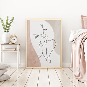 Może przedstawiać: Minimalistyczny wydruk liniowy przedstawiający dwie postaci, kt&oacute;re patrzą na siebie. Wydruk jest na jasnobeżowym tle z r&oacute;żowym akwarelowym rozmyciem. Rama jest w jasnym kolorze drewna.