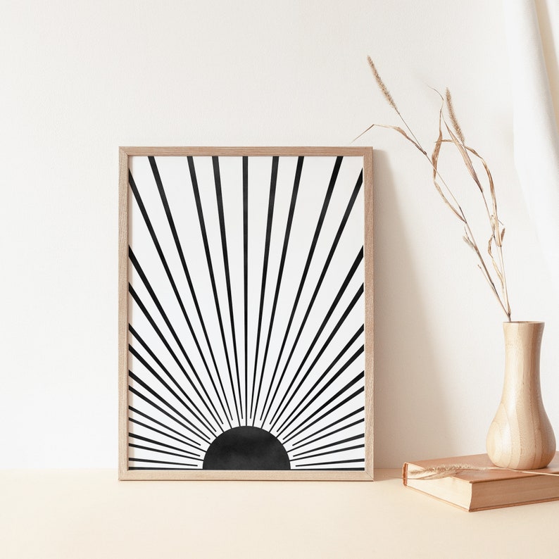 Op de afbeelding: Zwart-witte abstracte zonsondergang print in een houten lijst. De print toont een zwarte zon met stralende lijnen.