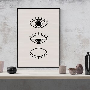 Puede incluir: Una impresi&oacute;n enmarcada en blanco y negro con tres ojos estilizados. Los ojos est&aacute;n dibujados en un estilo simple y minimalista. La impresi&oacute;n est&aacute; colgada en una pared blanca.
