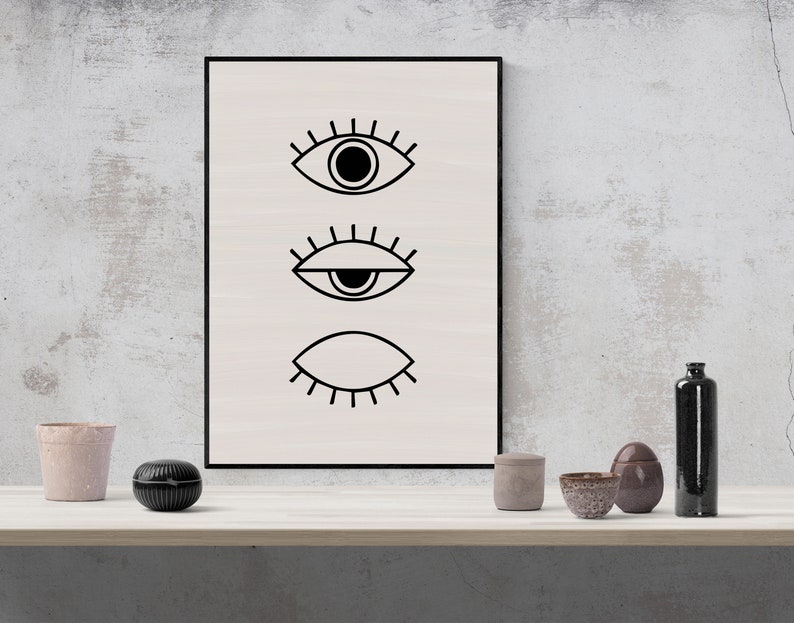 Puede incluir: Una impresi&oacute;n enmarcada en blanco y negro con tres ojos estilizados. Los ojos est&aacute;n dibujados en un estilo simple y minimalista. La impresi&oacute;n est&aacute; colgada en una pared blanca.