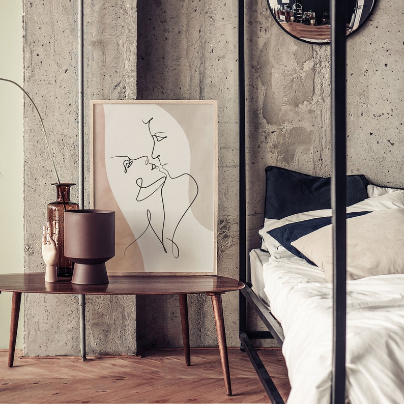 Może przedstawiać: Minimalistyczny wydruk sztuki liniowej przedstawiający dwie postaci w miękkiej r&oacute;żowo-beżowej kolorystyce. Wydruk jest oprawiony i wisi na ścianie nad drewnianym stolikiem kawowym.
