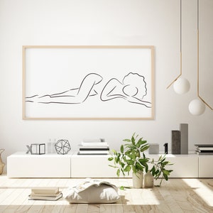 Puede incluir: Un dibujo en blanco y negro de una persona acostada, impreso sobre un fondo blanco y enmarcado en un marco de madera claro.