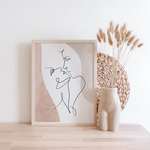 Może przedstawiać: Minimalistyczny wydruk sztuki liniowej przedstawiający dwie postaci całujące się, oprawiony w jasną drewnianą ramę. Wydruk ma beżowe tło i jest wyświetlany na jasnej drewnianej powierzchni.