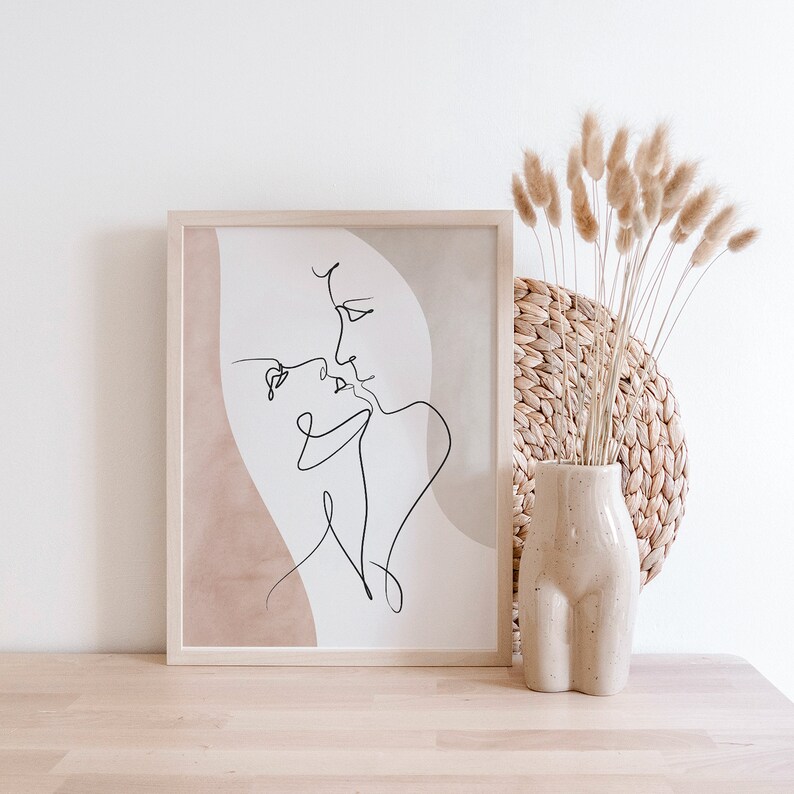 Może przedstawiać: Minimalistyczny wydruk sztuki liniowej przedstawiający dwie postaci całujące się, oprawiony w jasną drewnianą ramę. Wydruk ma beżowe tło i jest wyświetlany na jasnej drewnianej powierzchni.