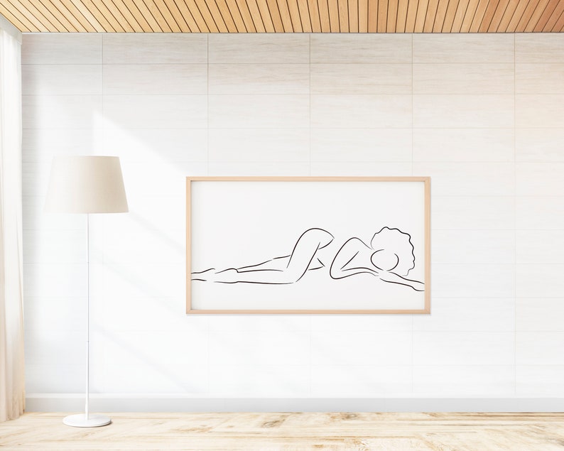Puede incluir: Un dibujo en blanco y negro de una persona acostada, enmarcado en un marco de madera clara, colgado en una pared de azulejos blancos.