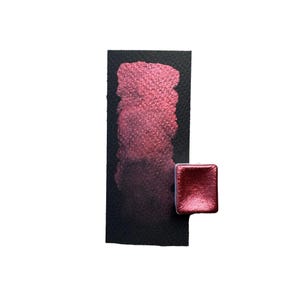 May include: A swatch of metallic red watercolor paint on black paper, with a matching square paint pan. The paint shows a gradient from light to dark red, with a shimmering, textured finish. The background is white.