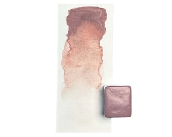 May include: A watercolor paint pan in a metallic rose gold color. The pan is shown next to a swatch of the color on watercolor paper.