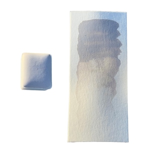 May include: A watercolor paint swatch on paper with a square paint block. The paint swatch shows a gradient of blue-gray hues. The square paint block is a light blue color.