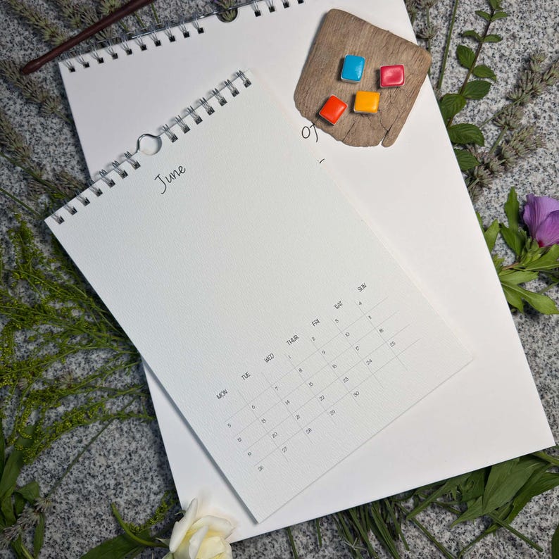 Größenvergleich: kleinerer Kalender mit Juniseite (Design Classic soft) liegt auf dem großen A3-Wandkalender 29,7 × 42 cm – mit Aquarellnäpfchen und Blumen