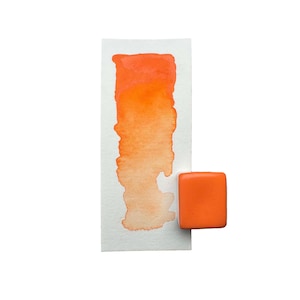 May include: A watercolour paint pan with a sample of orange watercolour paint on a white paper.