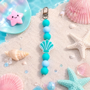 May include: A keychain featuring a silver-toned metal lobster clasp attached to a vertical string of alternating turquoise and light blue silicone beads, centered with a flat, stylized turquoise and white seashell-shaped silicone charm.