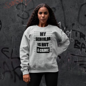 May include: A gray sweatshirt with black text that reads "My skin color is not a crime". The text is surrounded by a black and white ruler design.