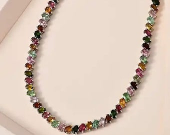 May include: A silver necklace featuring a row of colorful, oval-shaped gemstones. The gemstones are in shades of green, pink, yellow, orange, and purple. The necklace is displayed on a white surface.