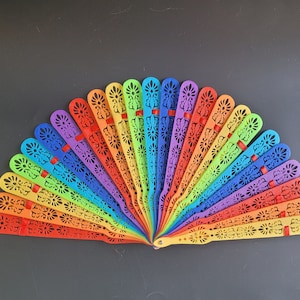May include: A rainbow fan of colourful plastic bracelets with intricate cut-out designs. Each bracelet is a different colour of the rainbow, starting with red and ending with yellow.