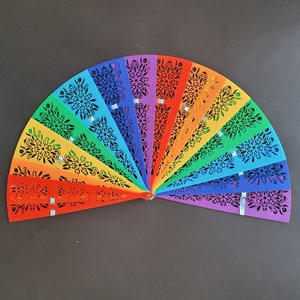 May include: A rainbow-coloured paper fan with a decorative cut-out design. Each section of the fan is a different colour of the rainbow, starting with red and ending with purple.