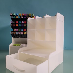 May include: White plastic desk organizer with a drawer and multiple compartments. The organizer is filled with colorful markers and pencils.