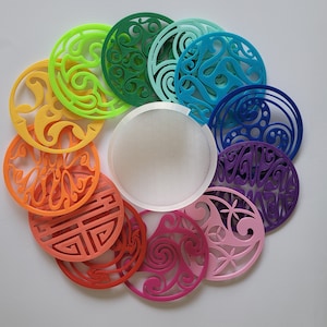 May include: A set of ten colourful coasters with intricate designs. The coasters are made of a hard plastic material and feature a variety of patterns, including swirls, geometric shapes, and floral motifs. The coasters are arranged in a circle, with a white circular base in the centre.
