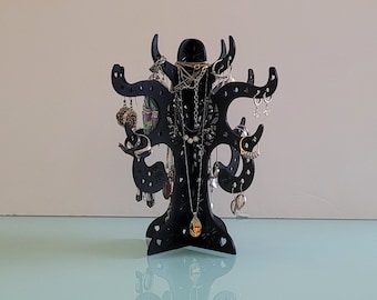 May include: A black jewelry tree stand with multiple branches and hooks for hanging necklaces, earrings, and bracelets. The stand is decorated with a heart pattern and has a small, round, decorative piece at the base.