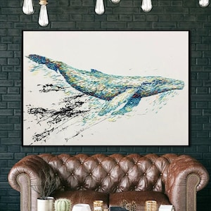 Könnte beinhalten: Gerahmtes Gemälde eines Wals in Blau-, Grün- und Gelbtönen vor weißem Hintergrund. Der Wal wird beim Schwimmen dargestellt, mit schwarzen Pinselstrichen, die Bewegung suggerieren. Das Kunstwerk hängt über einem braunen Ledersofa.